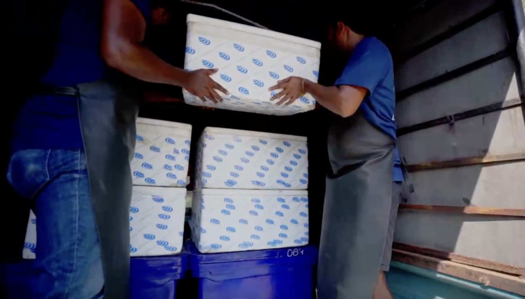 Two workers stacking white insulated cartons inside a vehicle